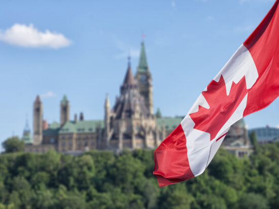Canadian flag waving with Parliament Buildings hill and Library